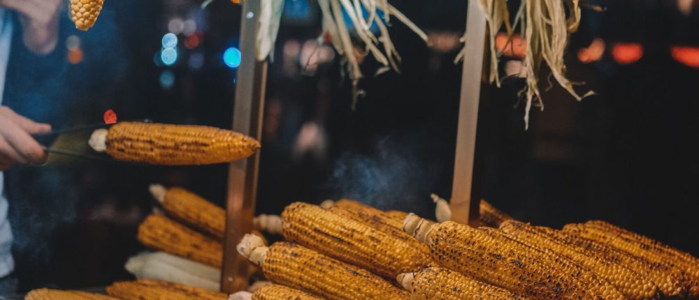 A vibrant display of hanging and stacked grilled corn under warm lights at an Istanbul street market.