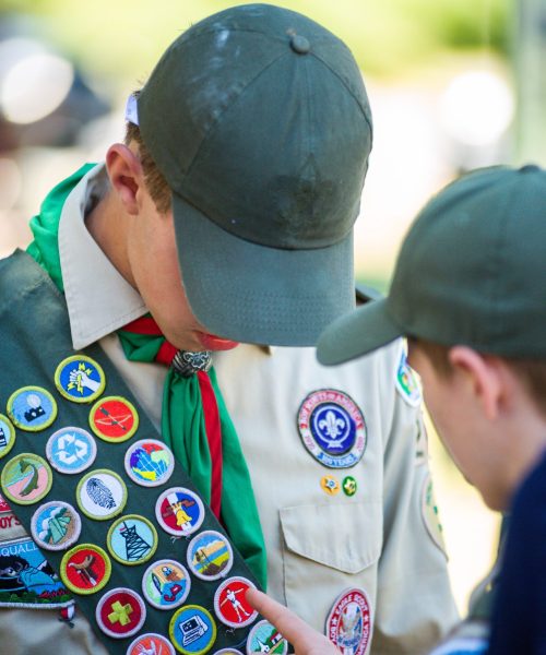 Two Boy Scouts examine merit badges on a sash, emphasizing achievements.